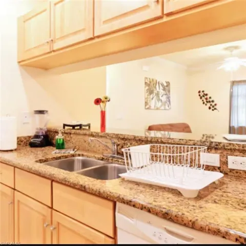 Kitchen featuring light wood cabinetry, granite-style countertops, and a double basin stainless steel sink