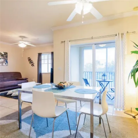 Open-concept dining area featuring a modern table, light-toned tile flooring, crown molding, and direct access to a balcony with metal railings