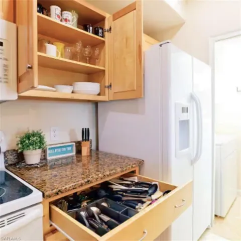 Kitchen area featuring light wood cabinetry, a mottled granite-finish countertop, and a white refrigerator with an ice and water dispenser