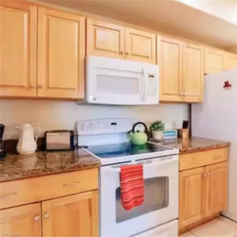 Kitchen featuring wood cabinetry, solid surface countertops, an over-the-range microwave, and a white electric range