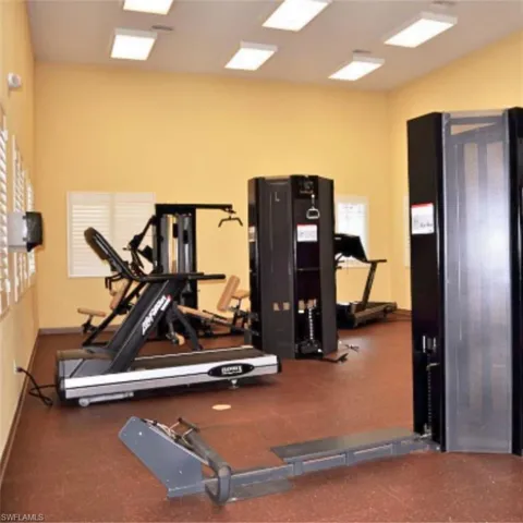 Dedicated fitness space featuring impact-absorbing flooring, multiple windows with louvered blinds, and recessed ceiling lighting