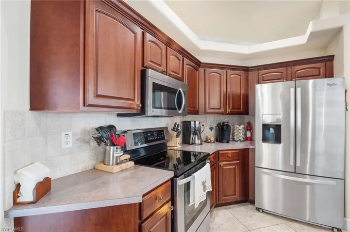 Kitchen featuring backsplash, a raised ceiling, light tile patterned floors, and appliances with stainless steel finishes