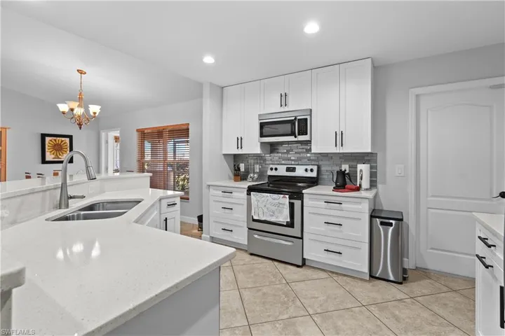 Kitchen with stainless steel appliances, white cabinets, recessed lighting, decorative light fixtures, and light stone counters