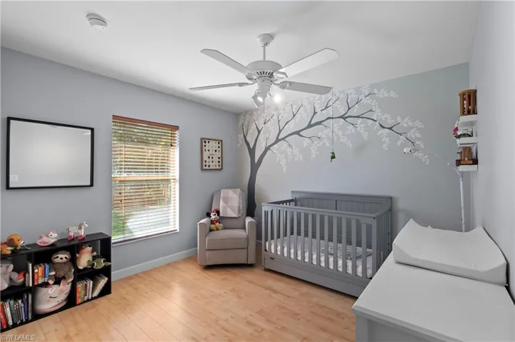 Bedroom featuring a crib, light wood-style floors, and a ceiling fan