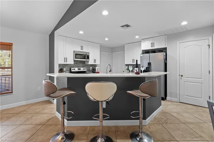 Kitchen with a kitchen bar, white cabinets, stainless steel appliances, recessed lighting, and tasteful backsplash