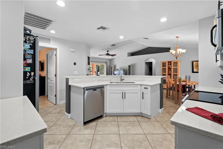 Kitchen featuring an island with sink, a chandelier, appliances with stainless steel finishes, light stone counters, and light tile patterned floors