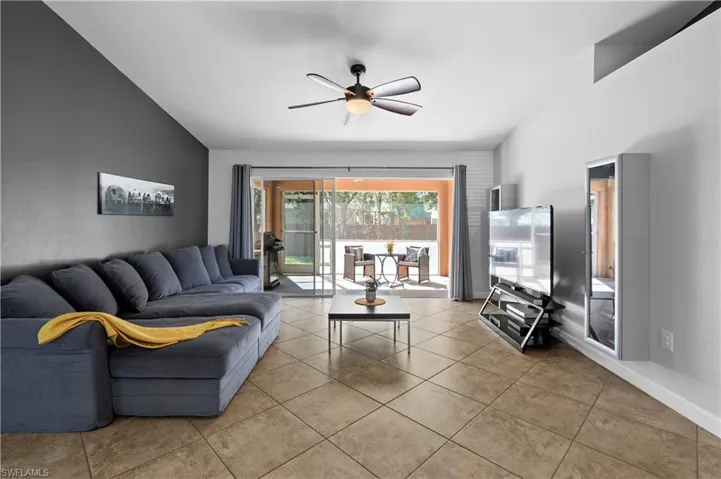 Living room with lofted ceiling, a ceiling fan, and light tile patterned flooring
