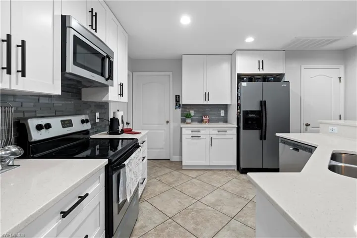 Kitchen featuring stainless steel appliances, white cabinetry, light stone countertops, and recessed lighting