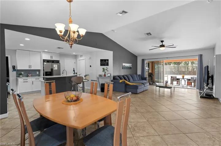 Dining space featuring vaulted ceiling, ceiling fan, light tile patterned flooring, and a chandelier
