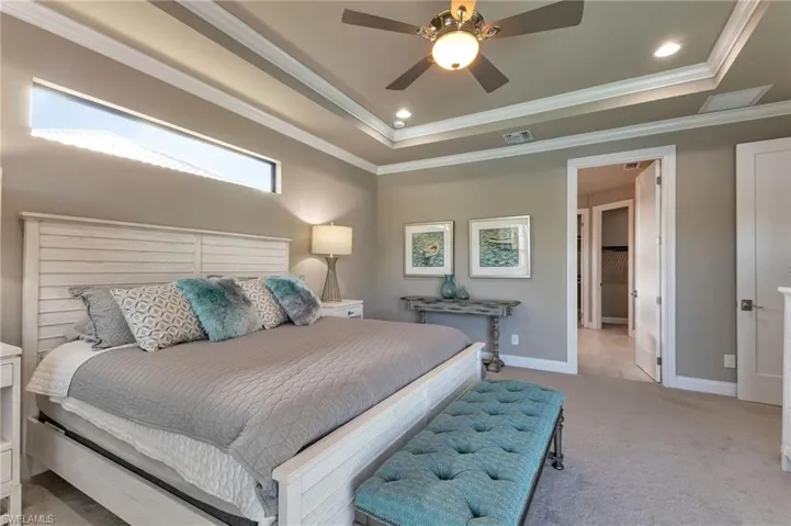 Carpeted bedroom with ornamental molding, ceiling fan, and a raised ceiling