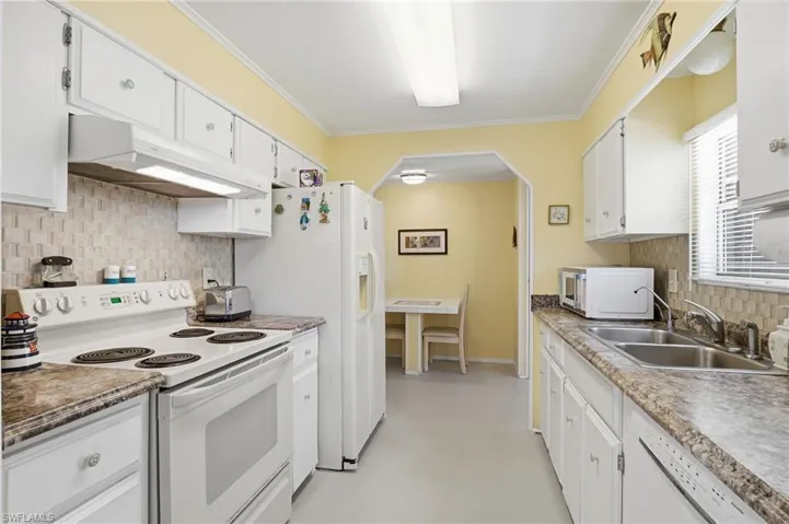 Kitchen with tasteful backsplash, white appliances, under cabinet range hood, white cabinets, and ornamental molding