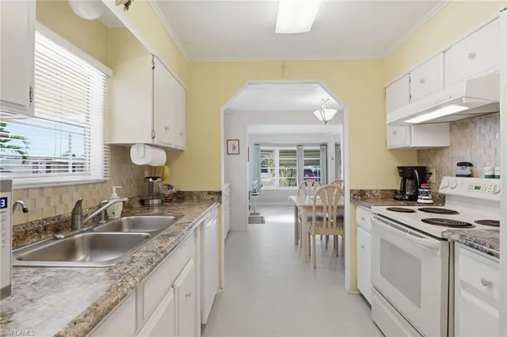Kitchen with white appliances, decorative backsplash, under cabinet range hood, crown molding, and white cabinets