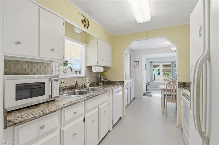 Kitchen featuring white appliances, white cabinets, healthy amount of natural light, crown molding, and arched walkways