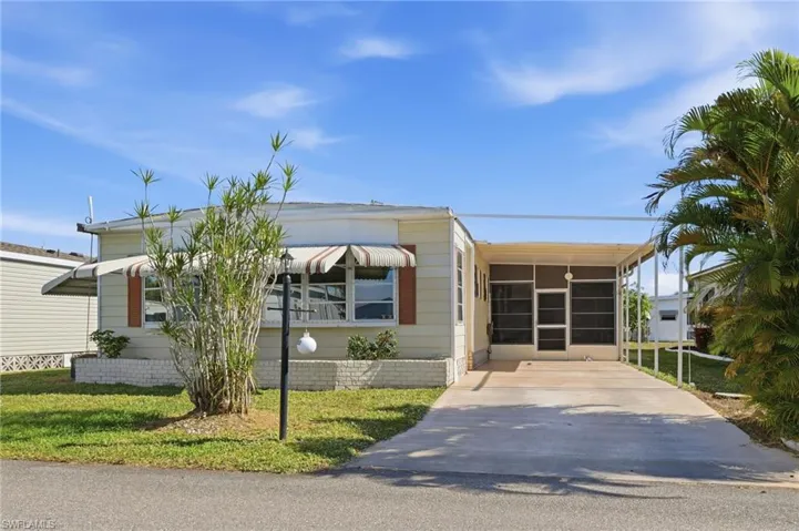 Manufactured / mobile home with a front yard, concrete driveway, a sunroom, and a carport