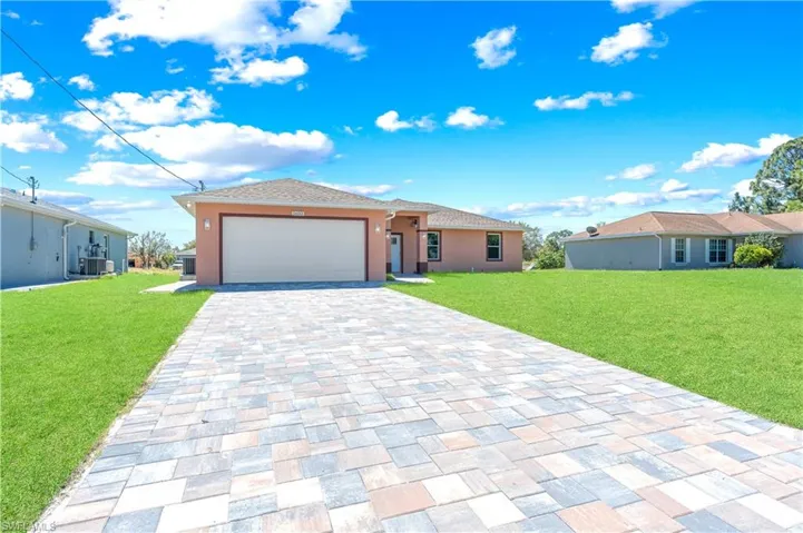 View of front of property featuring a front lawn, decorative driveway, a garage, and central AC