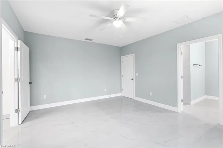 Unfurnished bedroom with baseboards, marble finish floor, ceiling fan, and a spacious closet