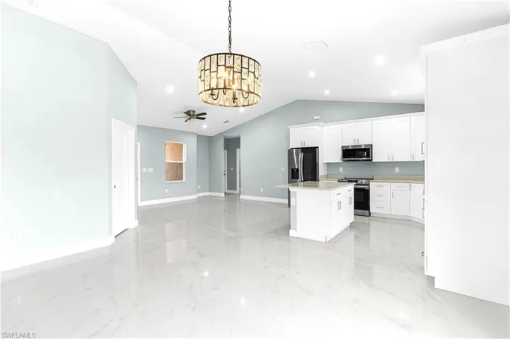 Kitchen featuring stainless steel appliances, light countertops, white cabinets, open floor plan, and a center island