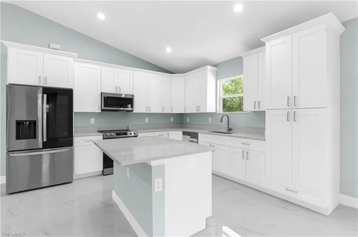 Kitchen with a sink, light stone counters, marble finish floor, and appliances with stainless steel finishes