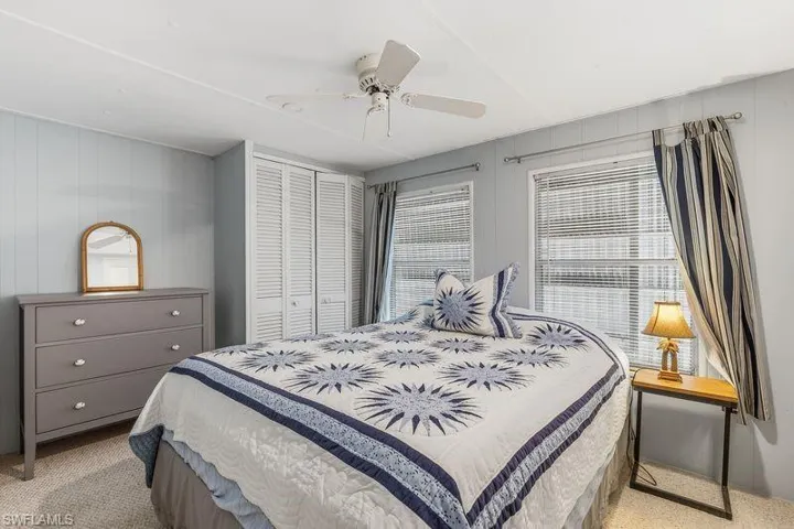 Bedroom featuring light blue paneling, two windows with blinds, a ceiling fan, and louvered bifold closet doors.