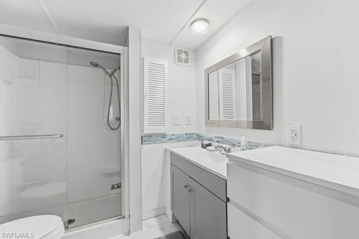Bathroom featuring a glass-enclosed shower, vanity with a white countertop, under-sink storage, a framed mirror, and a decorative tile backsplash, and tiled floors.