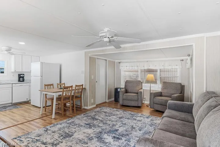 Open-concept living area featuring wood-finish laminate flooring, a ceiling fan, and white cabinetry in the kitchen space.