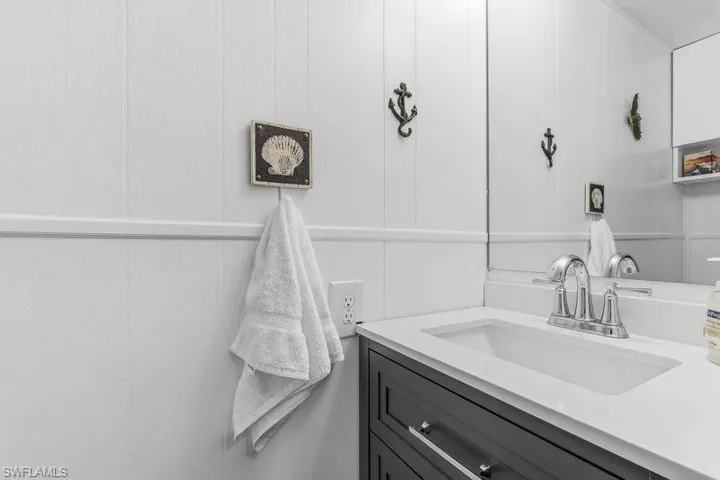 Half bath with white paneled walls that feature a built-in vanity with a white countertop and toilet.