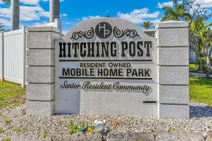Entrance sign for "Hitching Post Resident Owned Mobile Home Park" with textured stone columns and a decorative arched top.