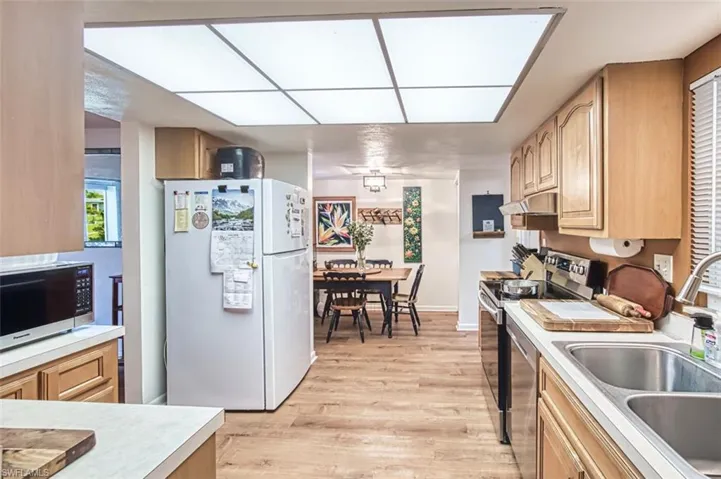 Kitchen with stainless steel appliances, light countertops, light brown cabinetry, light wood-style floors, and under cabinet range hood