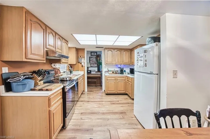 Kitchen with electric range, freestanding refrigerator, under cabinet range hood, light wood-type flooring, and light countertops