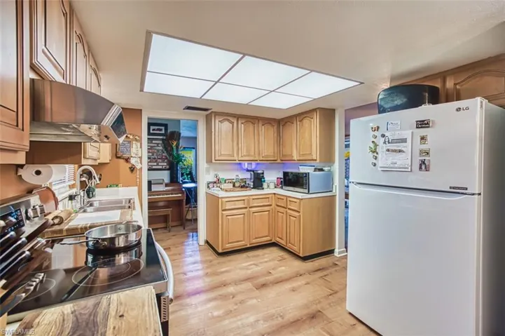 Kitchen with appliances with stainless steel finishes, extractor fan, light wood-style flooring, and light countertops