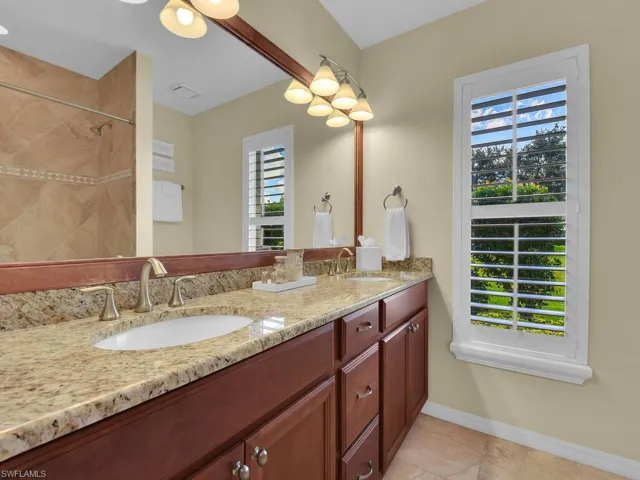 Bathroom with a wealth of natural light, tile patterned flooring, vanity, and tiled shower