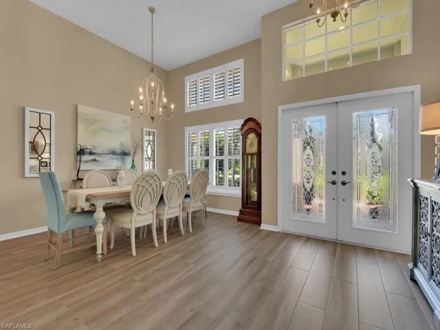 Dining space with light hardwood / wood-style flooring, a towering ceiling, a chandelier, and french doors