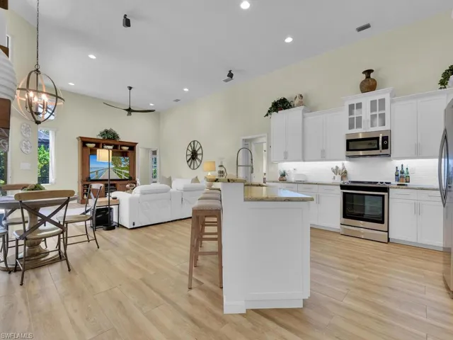 Kitchen featuring light wood-type flooring, an island with sink, white cabinetry, stainless steel appliances, and decorative light fixtures