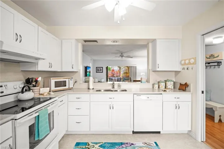 Kitchen featuring white appliances, under cabinet range hood, ceiling fan, a sink, and light countertops