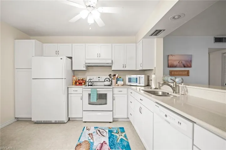 Kitchen with white appliances, under cabinet range hood, a sink, light countertops, and white cabinetry