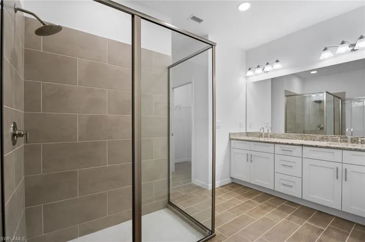 Bathroom with double vanity, a shower stall, recessed lighting, and a walk in closet