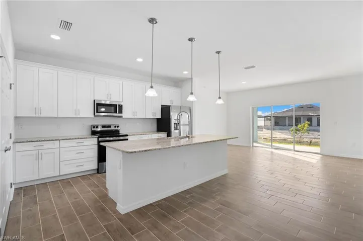 Kitchen with stainless steel appliances, light stone countertops, a kitchen island with sink, and white cabinets