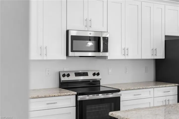Kitchen with stainless steel appliances, white cabinetry, and light stone countertops