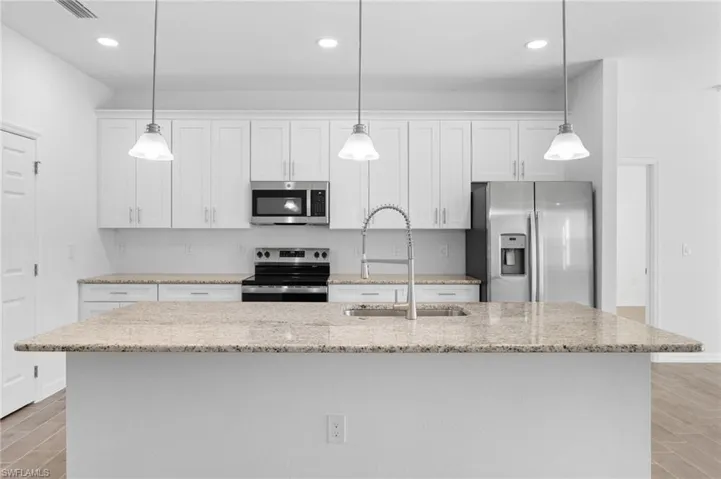 Kitchen with wood finish floors, stainless steel appliances, white cabinets, light stone counters, and hanging light fixtures