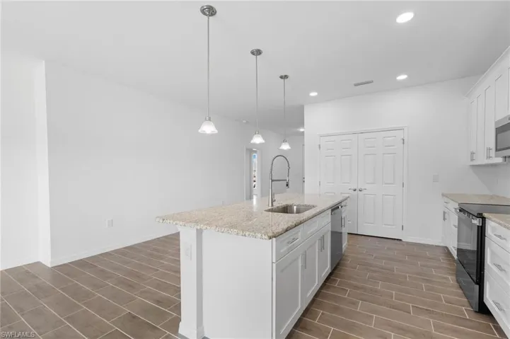Kitchen featuring white cabinets, stainless steel appliances, decorative light fixtures, light stone counters, and an island with sink