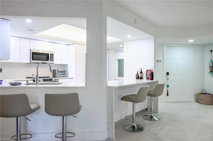 Kitchen with a kitchen breakfast bar, white cabinetry, recessed lighting, a peninsula, and stainless steel microwave