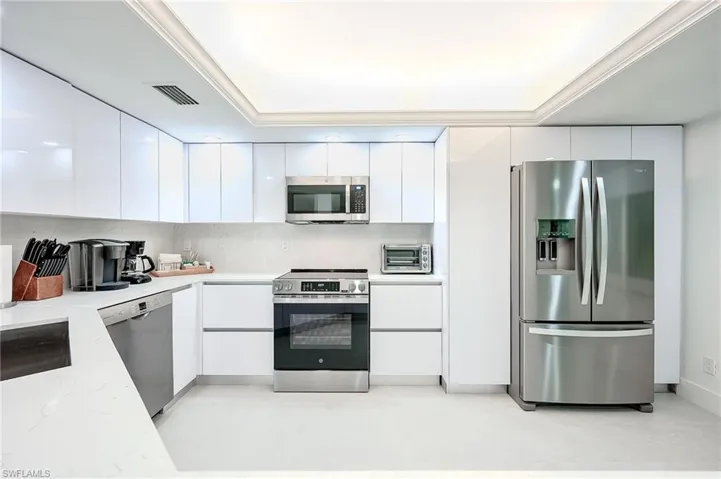 Kitchen featuring stainless steel appliances, white cabinetry, modern cabinets, tasteful backsplash, and light stone countertops