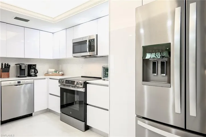 Kitchen with modern cabinets, white cabinets, stainless steel appliances, light countertops, and ornamental molding