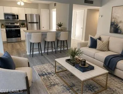 Open-concept living space with wood-finish flooring, white cabinetry, stainless steel appliances, and a breakfast bar