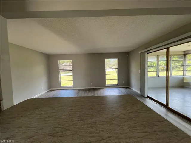 Empty room featuring a textured ceiling, a wealth of natural light, and dark wood-type flooring