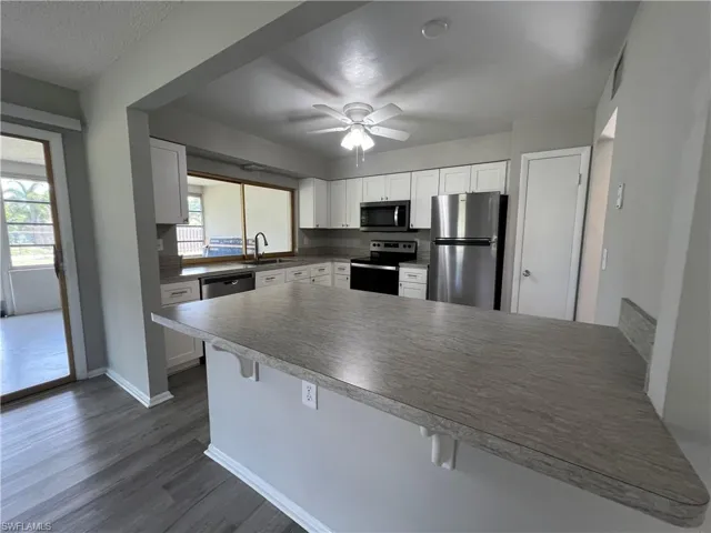 Kitchen featuring dark wood-type flooring, appliances with stainless steel finishes, a breakfast bar area, sink, and ceiling fan