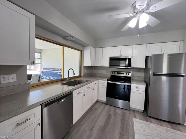 Kitchen featuring stainless steel appliances, wood-type flooring, sink, and white cabinets