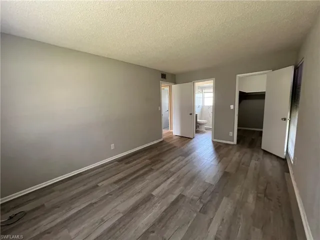 Unfurnished bedroom with a closet, ensuite bathroom, dark hardwood / wood-style flooring, and a spacious closet