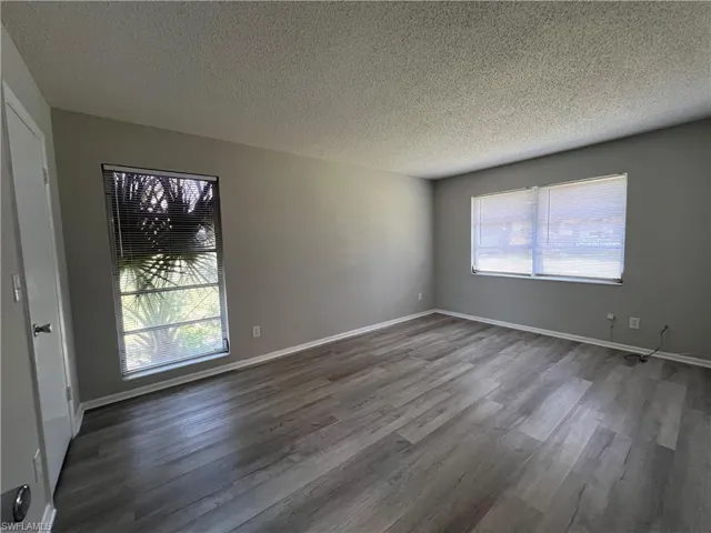 Empty room with a textured ceiling and dark hardwood / wood-style flooring