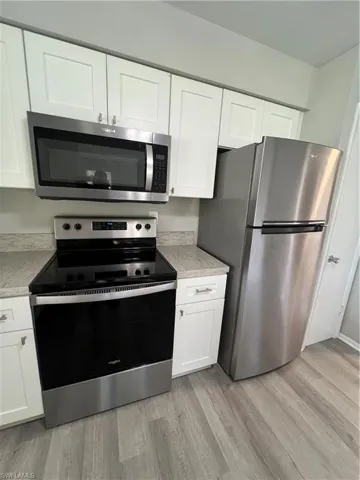 Kitchen with white cabinets, light wood-type flooring, stove, and fridge